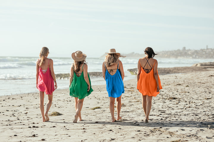 Four women walking away from camera on beach, wearing Bette Amalie mini cover ups in multiple colors