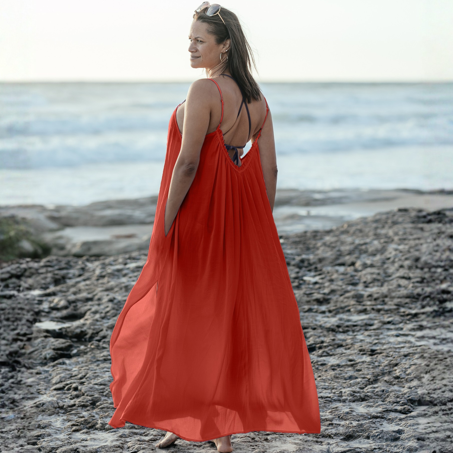 Woman standing at the ocean edge looking off into the distance wearing a coral dress.