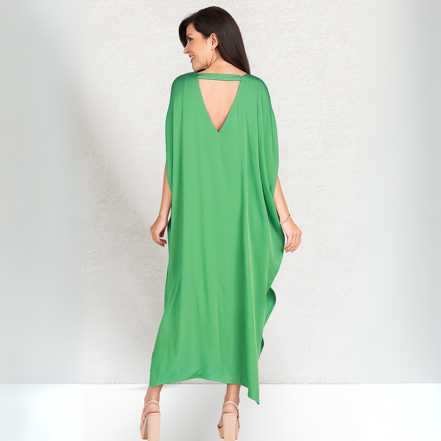 Back view of a woman wearing a green caftan in a white background studio.