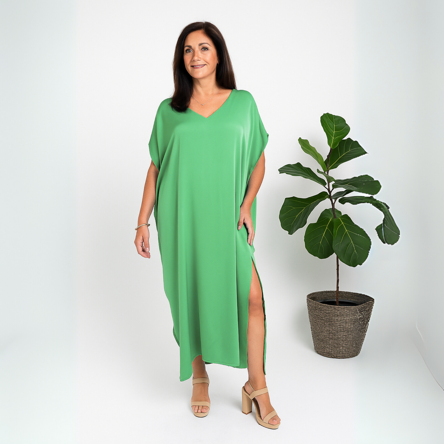 Front view of a woman in a green caftan standing in a white studio with a fig tree behind her.