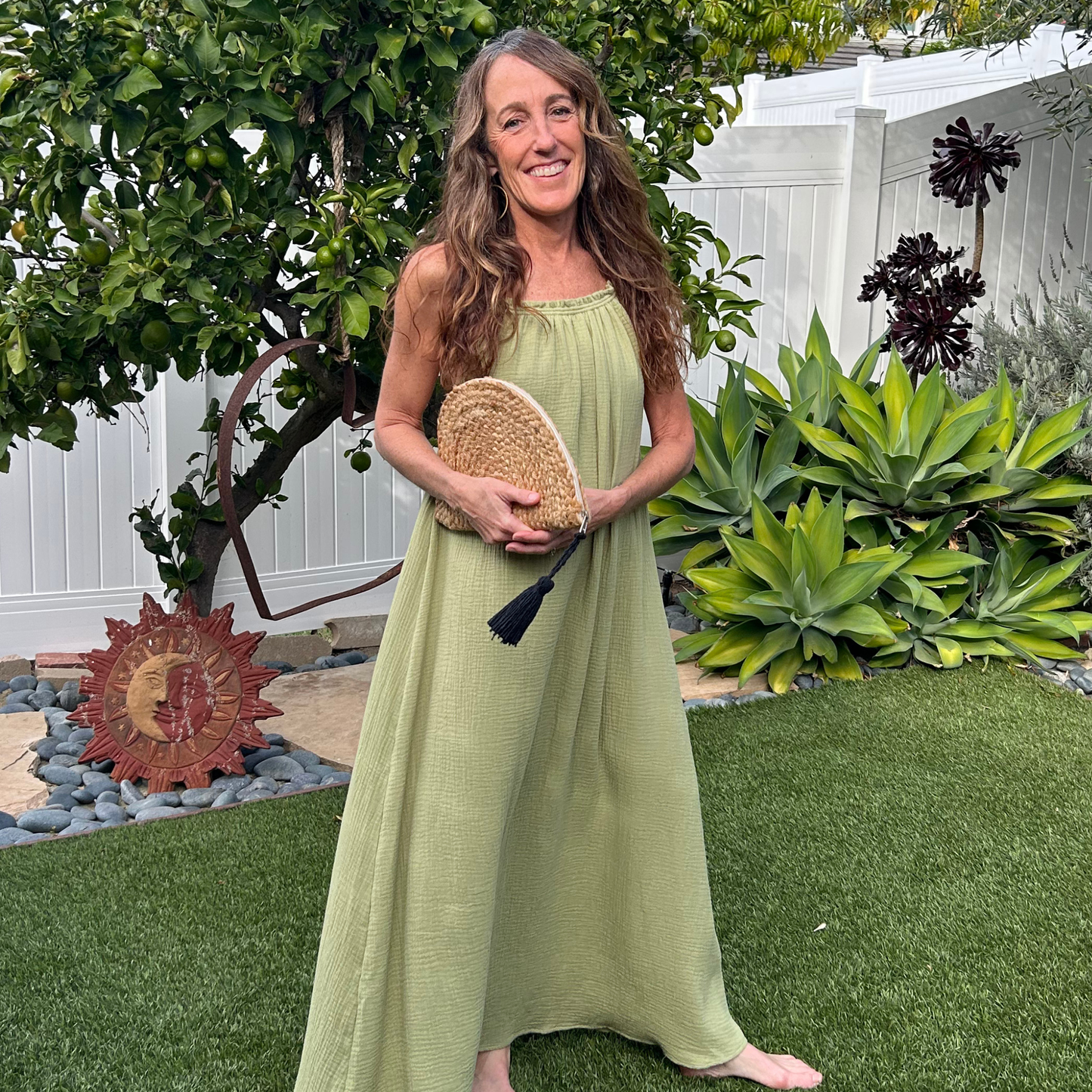 Woman in a green dress holding a woven bag in a garden setting