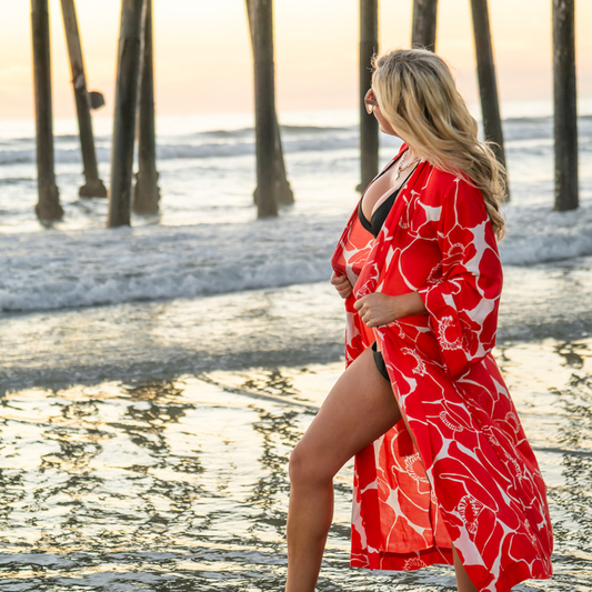 Woman in a red floral cover-up standing on a beach with sunset in the background