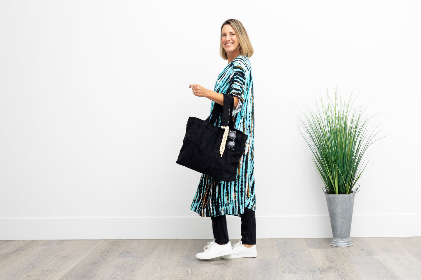 Woman walking and smiling wearing a long turquoise and black kimono, carrying a black bag.