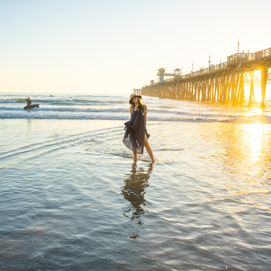 Woman walking on a beach at sunset with a pier in the background
