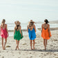 Four women walking away from camera on beach, wearing Bette Amalie mini cover ups in multiple colors