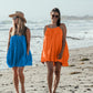 Two women walking towards camera on the beach, wearing Bette Amalie mini beach cover ups in ocean blue and citrus colors