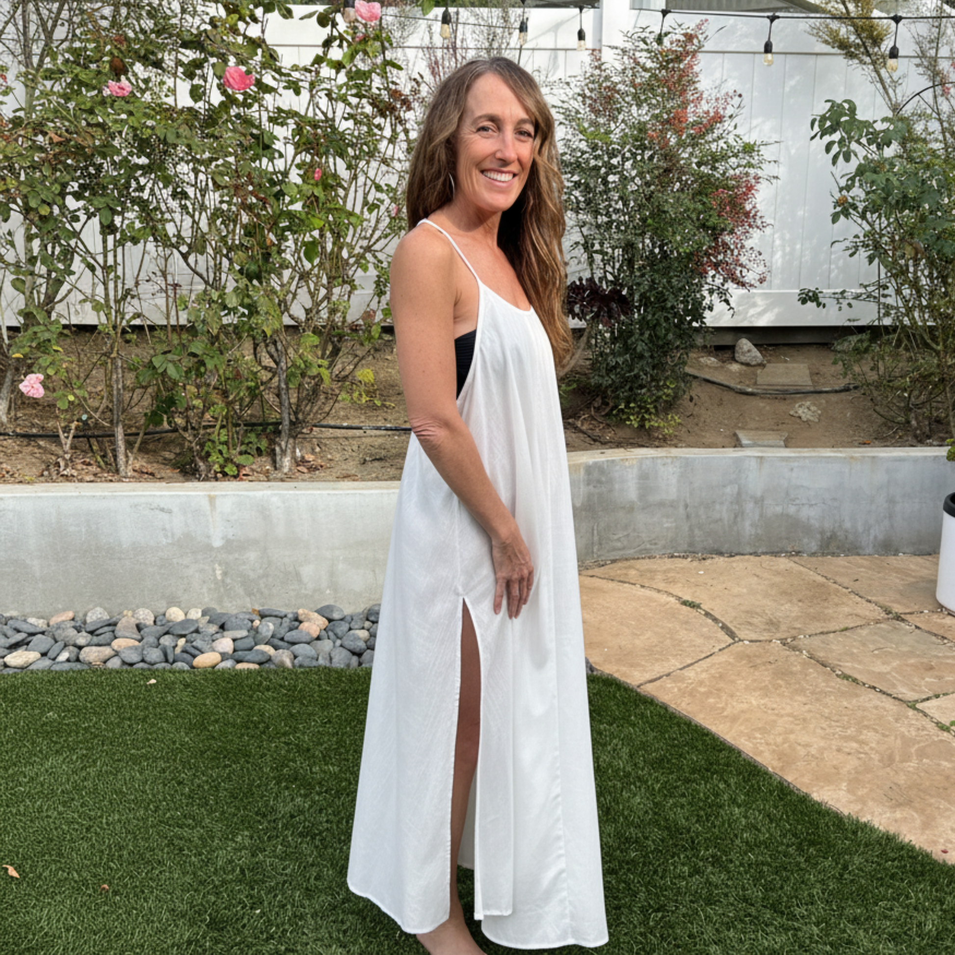 Woman in a white linen maxi dress standing outdoors with greenery and a white wall in the background