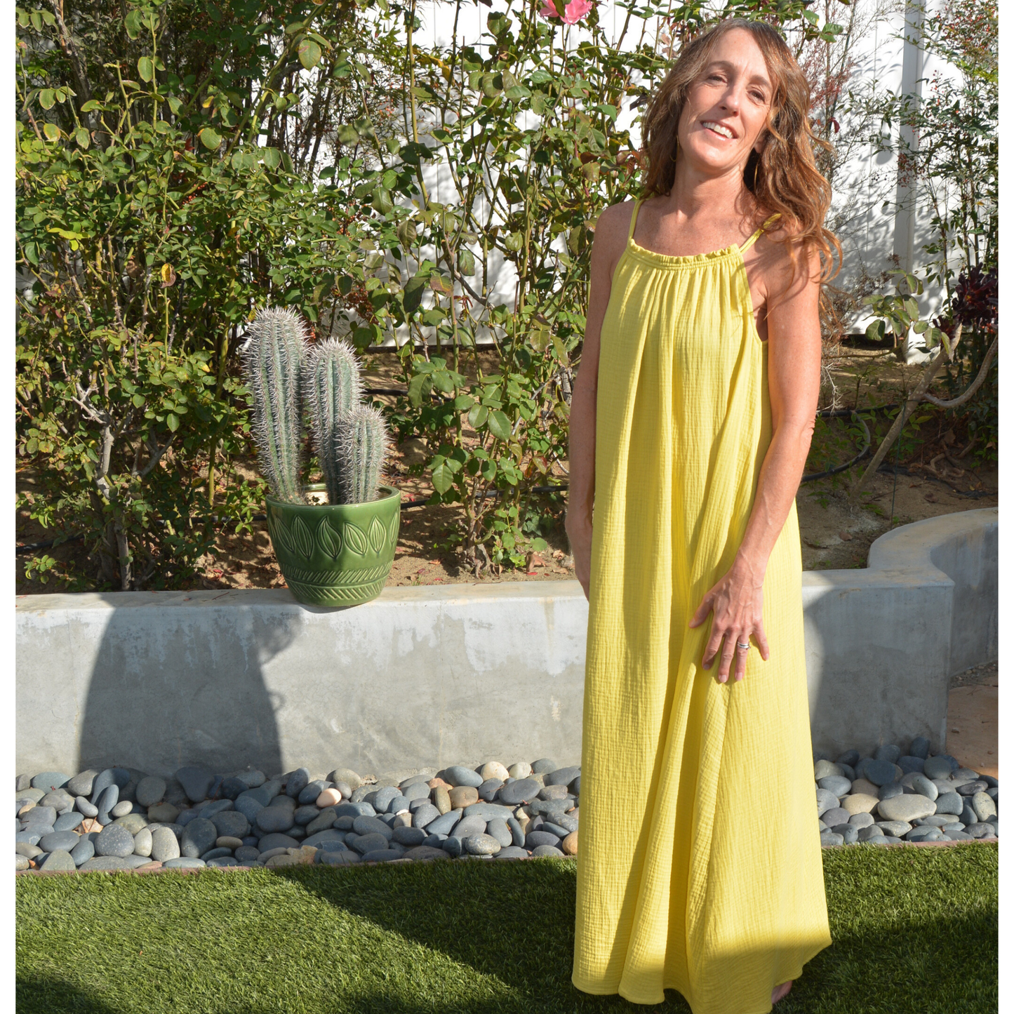 Woman in a yellow maxi dress standing in a garden with plants and rocks.
