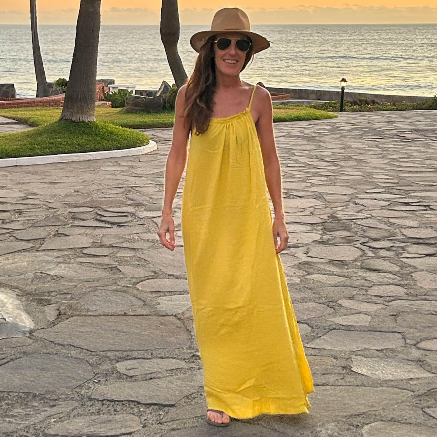 Woman in a yellow dress standing on a cobblestone street near the ocean.