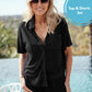 A woman wearing a black short-sleeve button-front top and matching black shorts stands by a pool with a blurred outdoor background. A blue circular badge in the top right reads 'Top & Shorts Set'.
