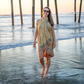 Woman in a yellow dress standing on a beach with water up to her ankles.