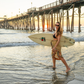 Woman holding a surfboard walking on a beach with a pier in the background