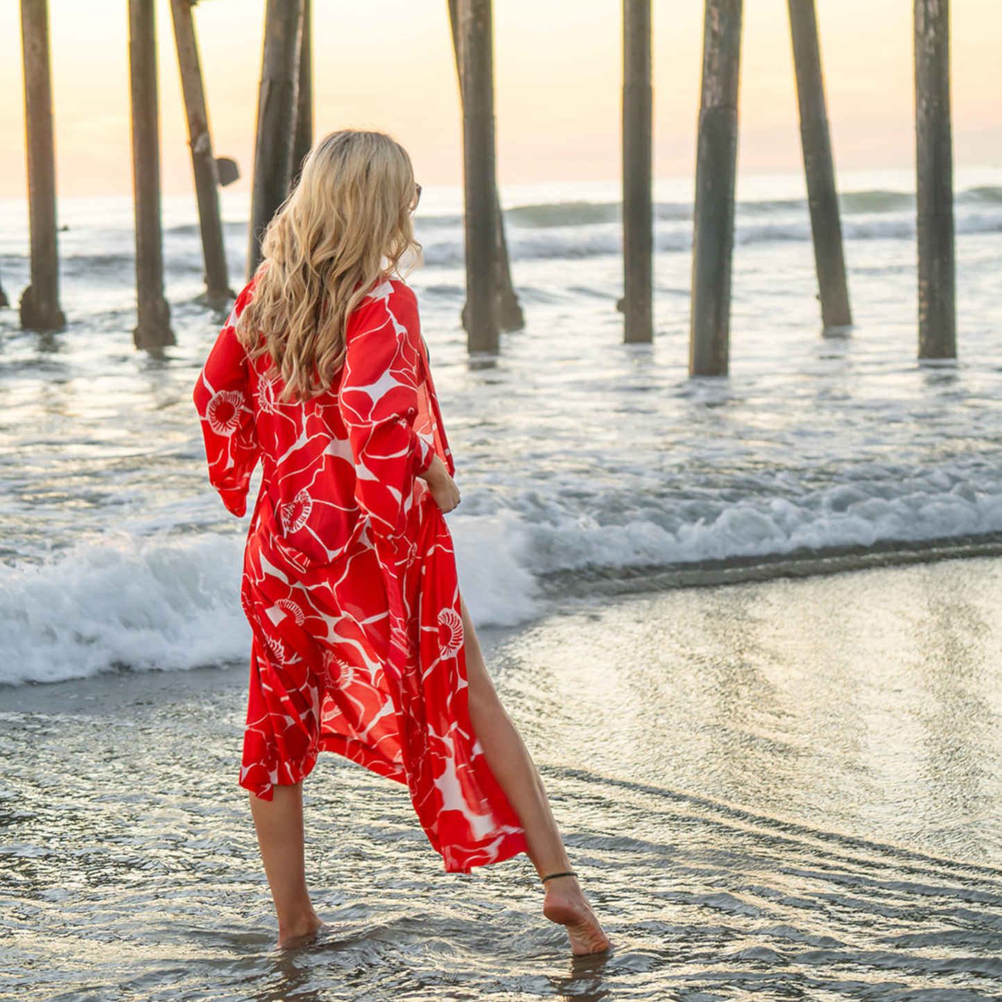 Woman in a red and white floral kimono walking along a beach at sunset.