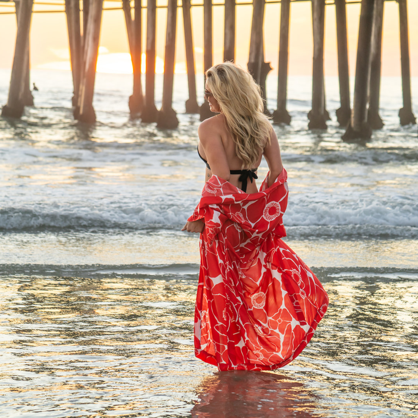 Woman in a red and white kimono standing on a beach with a pier in the background