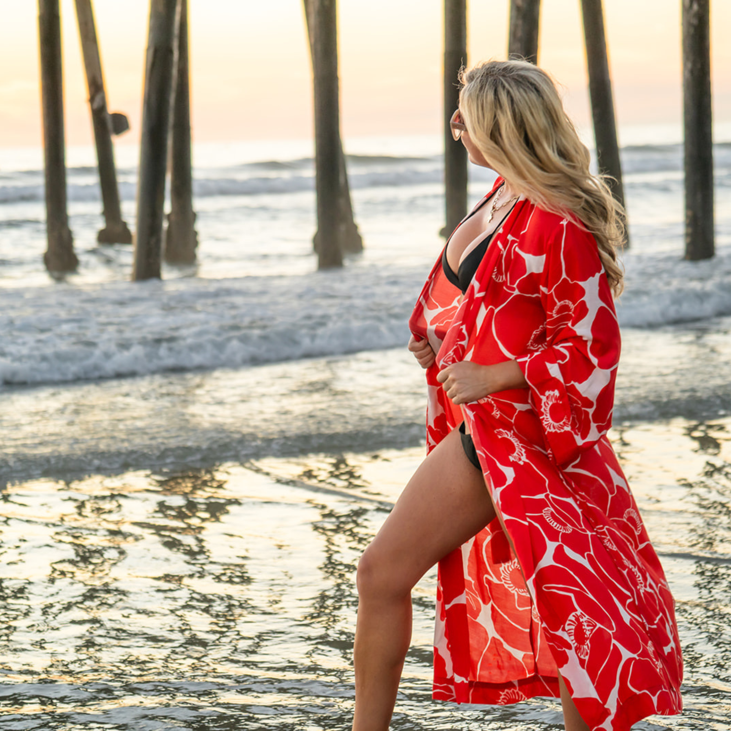 Woman in a red floral cover-up standing on a beach with sunset in the background