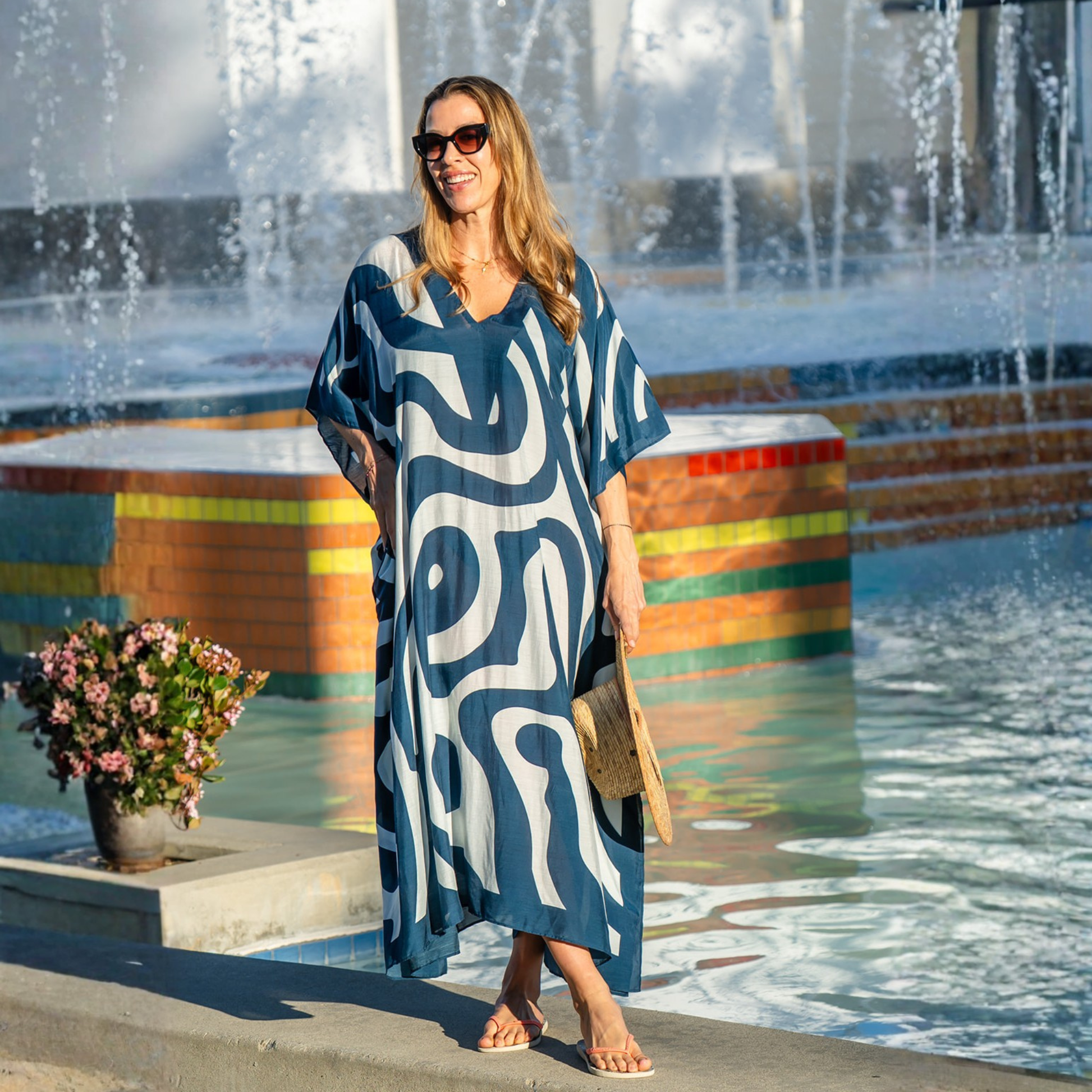 Woman in a blue and white patterned kaftan standing in front of a fountain.