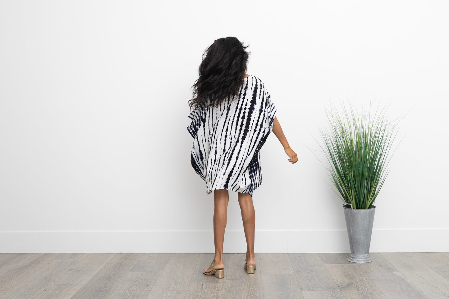Back of a woman twirling in a blue and white short caftan wearing gold sandals.