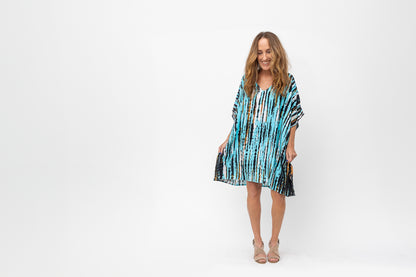 Woman looking down and laughing wearing in a turquoise, black and white short caftan.