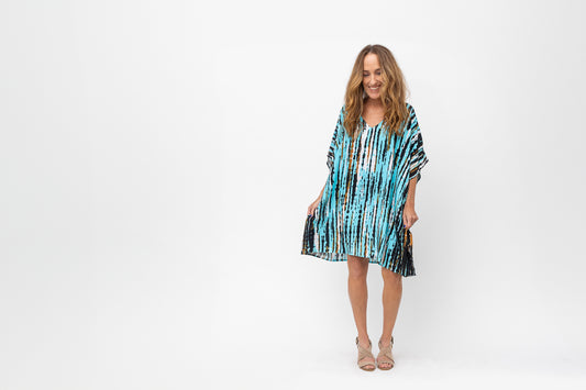Woman looking down and laughing wearing in a turquoise, black and white short caftan.