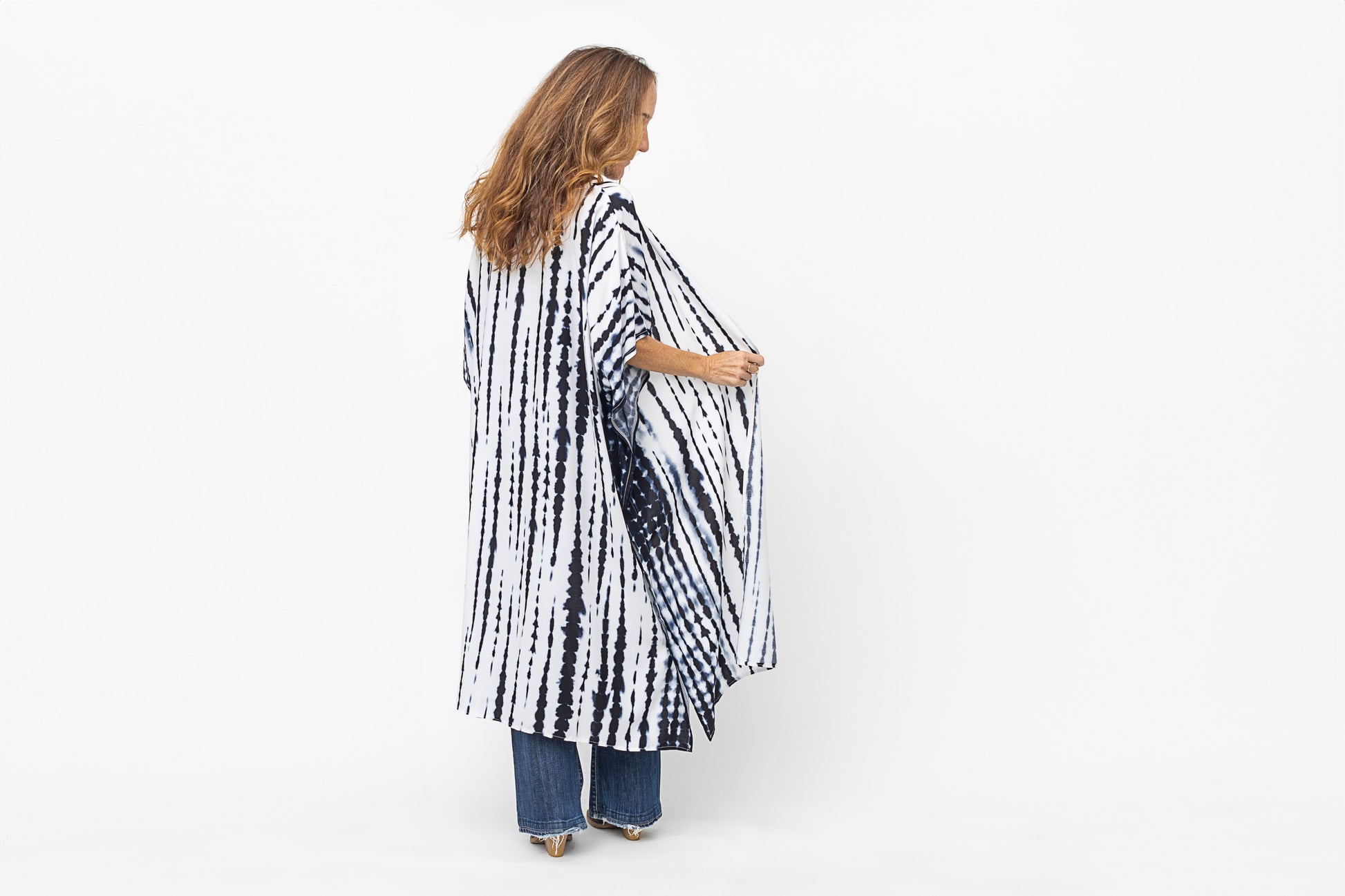 Woman turning around in jeans and a long blue and white kimono.