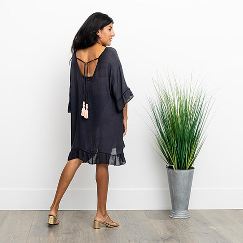 Woman with back to camera in black cover up dress, looking over her shoulder.