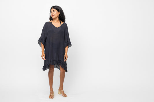 Woman standing, wearing black cover up dress, looking off to the distance.