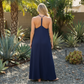 woman standing in a yard facing backwards wearing a navy blue maxi dress.