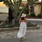 Woman in a white dress and hat walking along a stone path near a cactus plant with a scenic background.