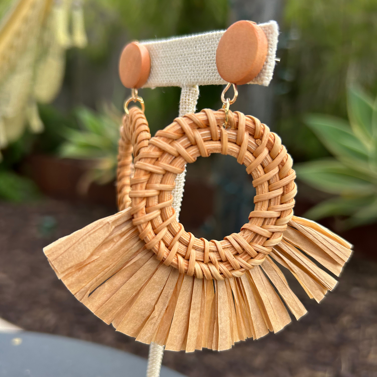 Woven raffia earring with tassels on a blurred natural background