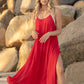 Woman standing on the beach with boulders behind her in a red dress. The breeze is blowing her dress.