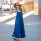 Woman in a blue dress and sun hat standing on a sidewalk.