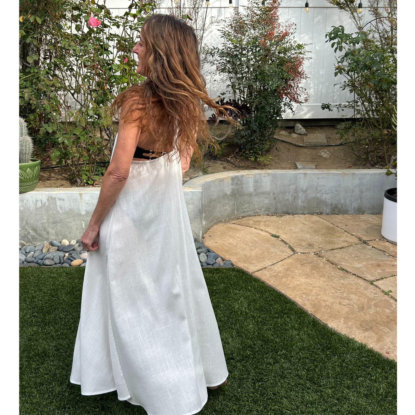 Woman in a white linen dress standing in a garden with greenery and a pool in the background