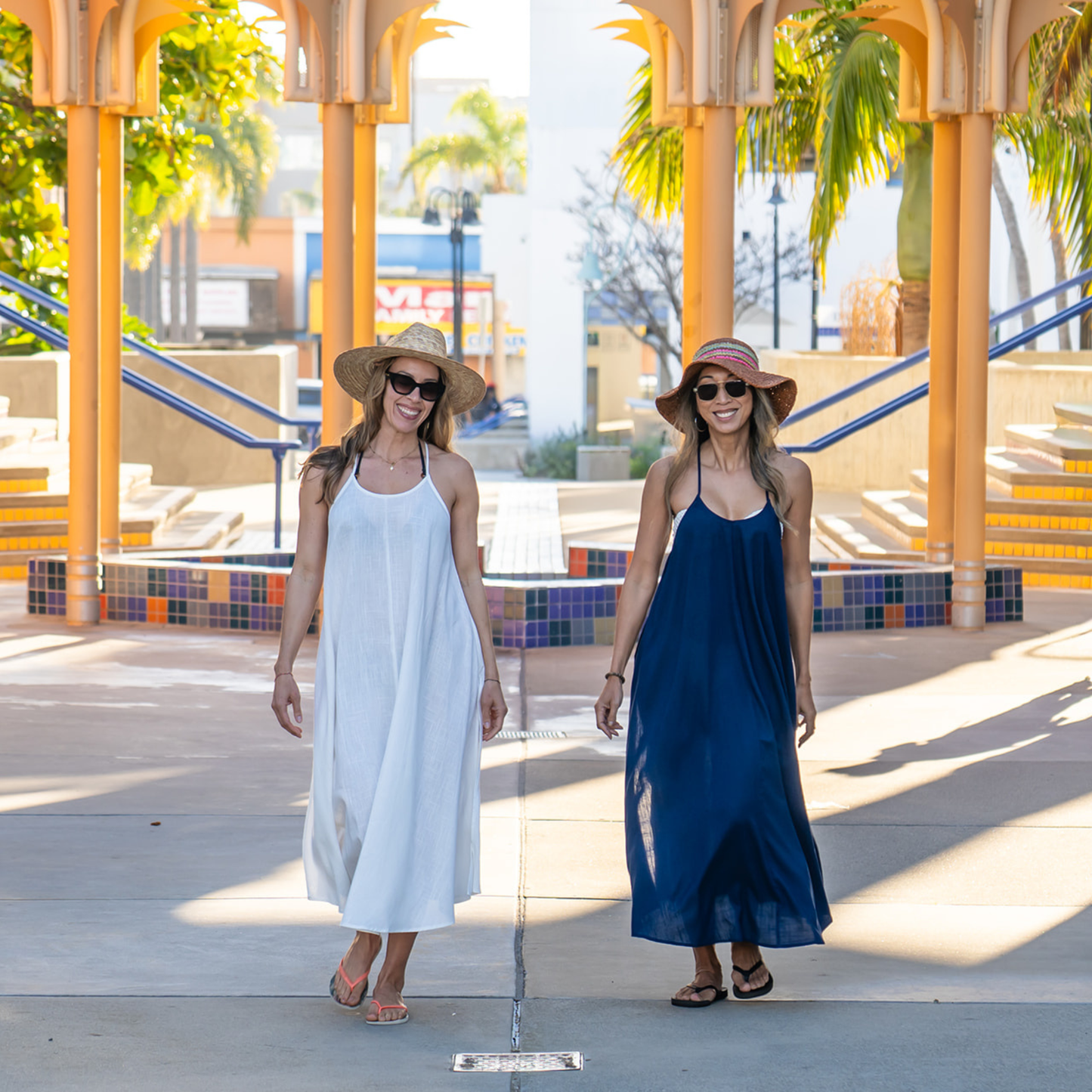 Two women in dresses standing in front of a reflective surface with a colorful architectural background.