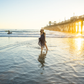 Woman walking on a beach at sunset with a pier in the background
