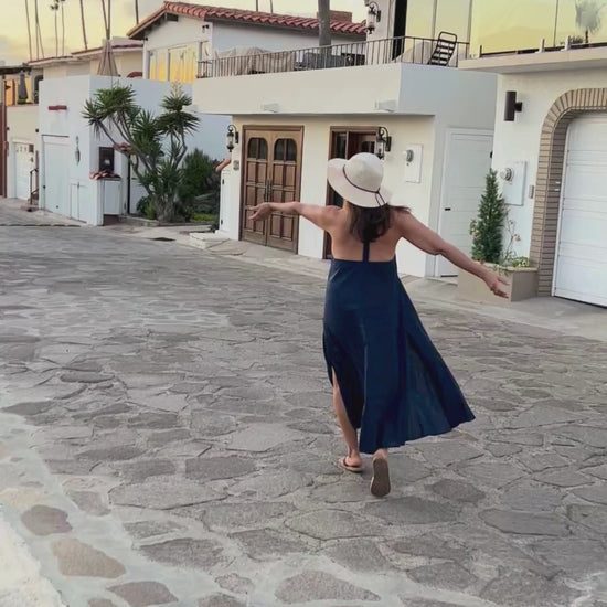 Woman walking and dancing in a blue dress down a cobblestone street.