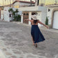 Woman walking and dancing in a blue dress down a cobblestone street.