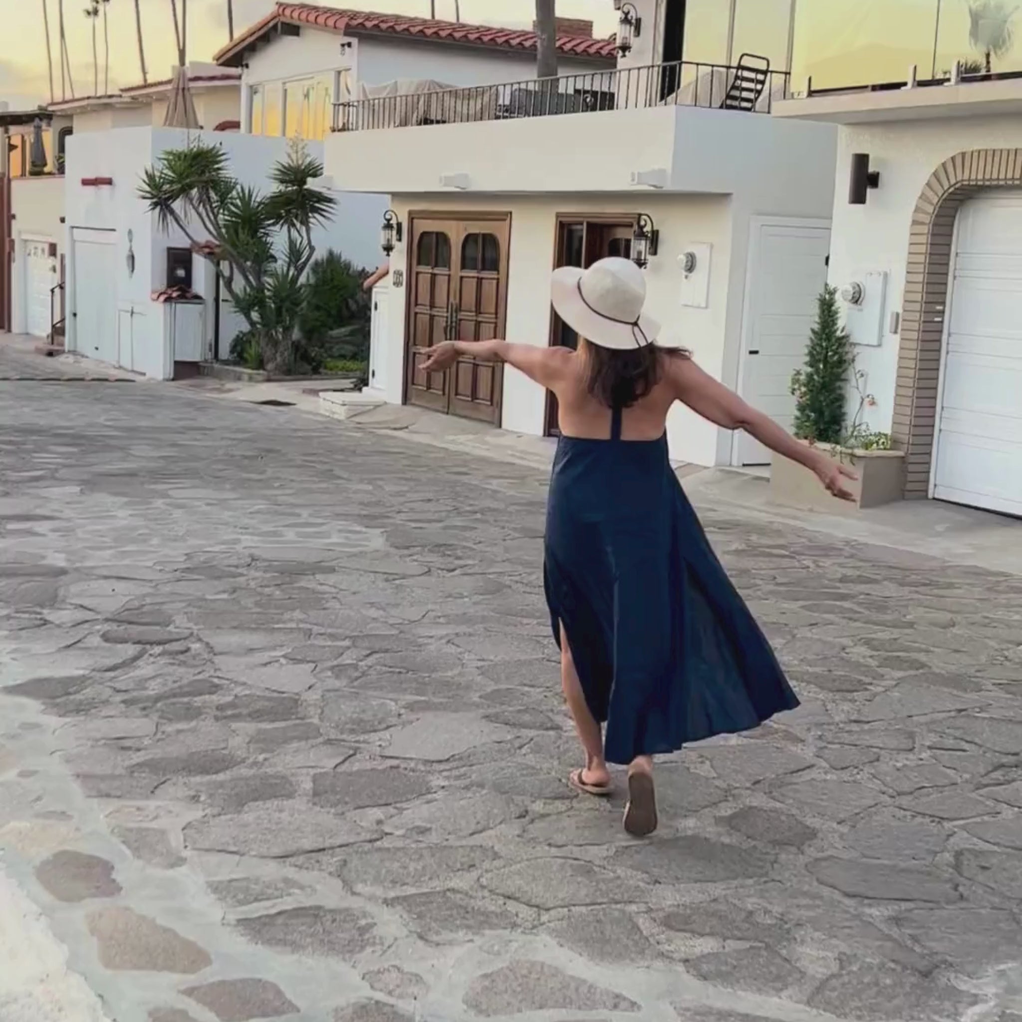 Woman walking and dancing in a blue dress down a cobblestone street.