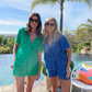 Two women posing in a green and a blue matching shorts set standing in front of a tropical pool.