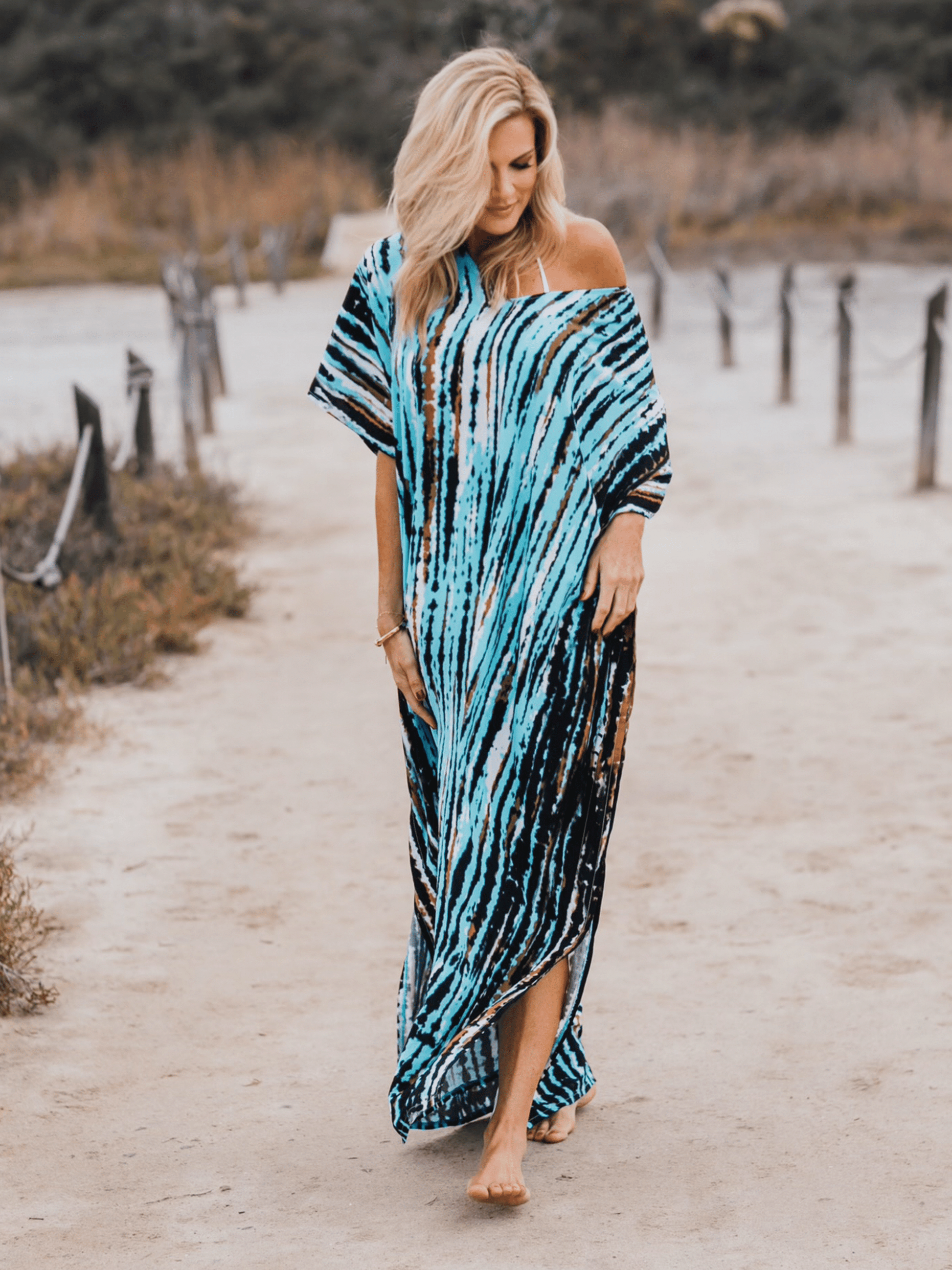 Woman walking on a sandy path wearing a tie dyed turquoise caftan.