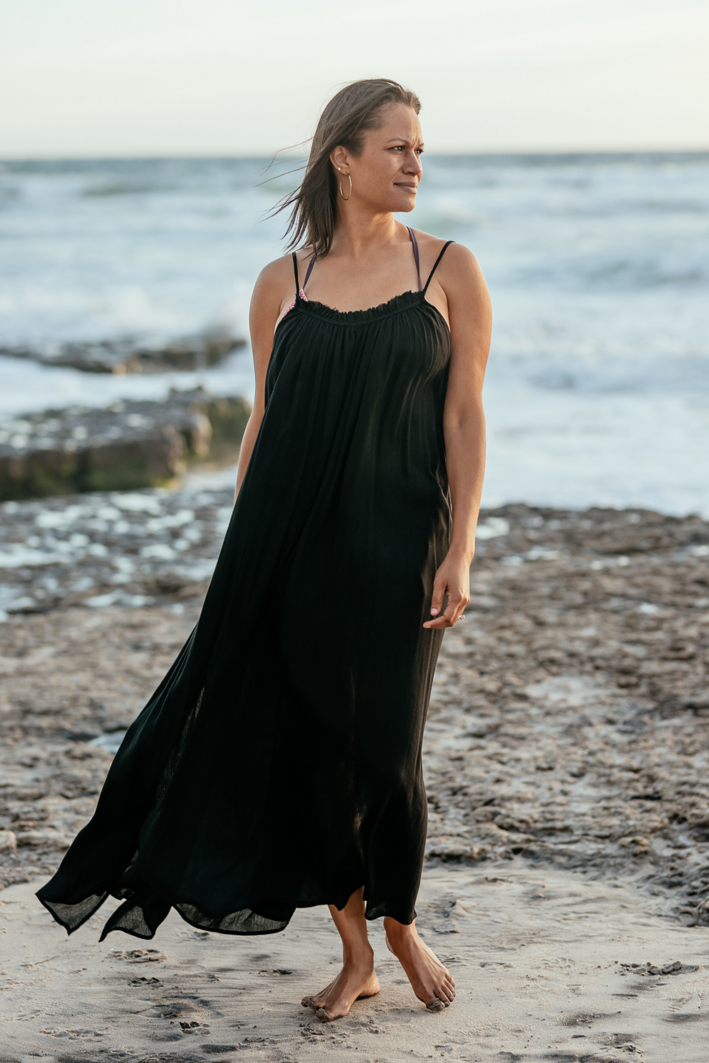 Woman wearing black Bette cover up dress on the beach in the breeze so you can see how fabric flows.