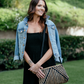 Woman wearing black jumpsuit paired with jean jacket and jute purse.