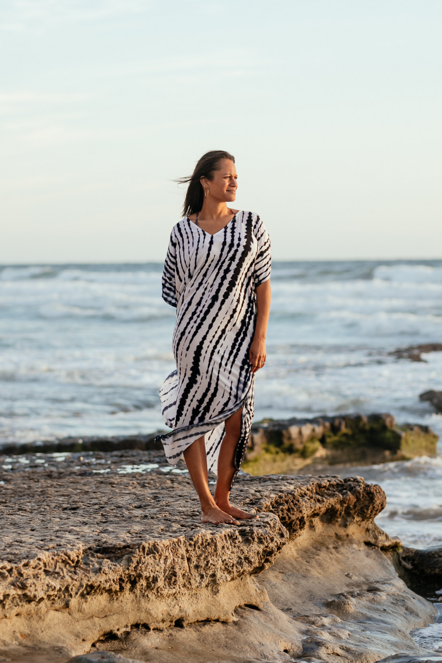 woman standing at low tide looking out at the water. She's wearing a tie dyed, blue and white long caftan dress.