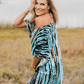 Woman in tie dyed caftan turned sideways towards the camera, looking over her shoulder. She is in a field.