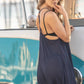 Woman standing in front of a VW van, flirting with the camera in a blue coverup dress.