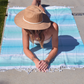 Woman sunbathing on a blue and green striped towel wearing a hat.