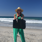Woman on a beach wearing a green jumpsuit, holding a black bag.