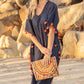 Woman wearing blue caftan and carry a colorful clutch at the beach.