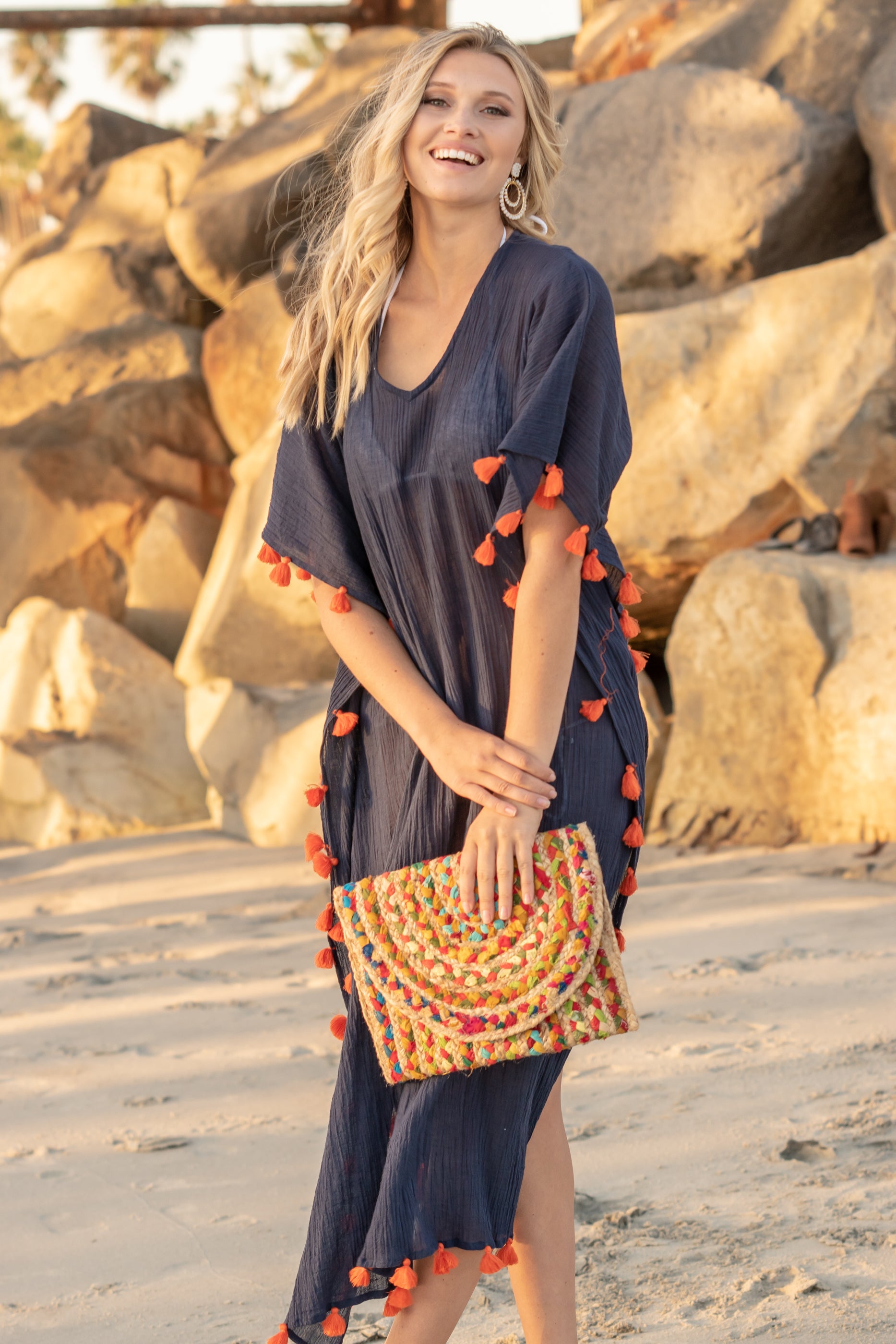 Woman wearing blue caftan and carry a colorful clutch at the beach.